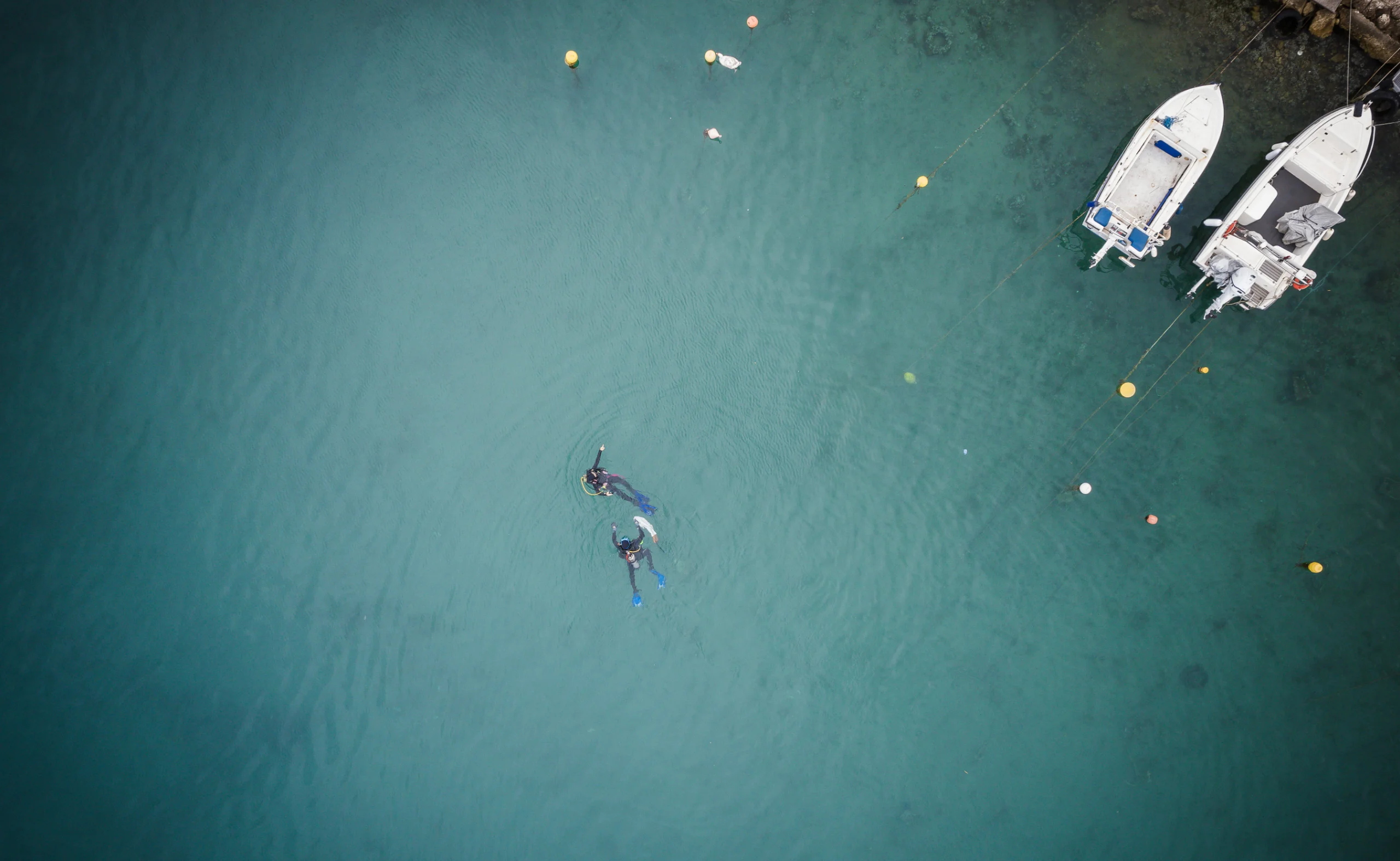 wo divers performing underwater cleanup near docked boats in clear blue sea.